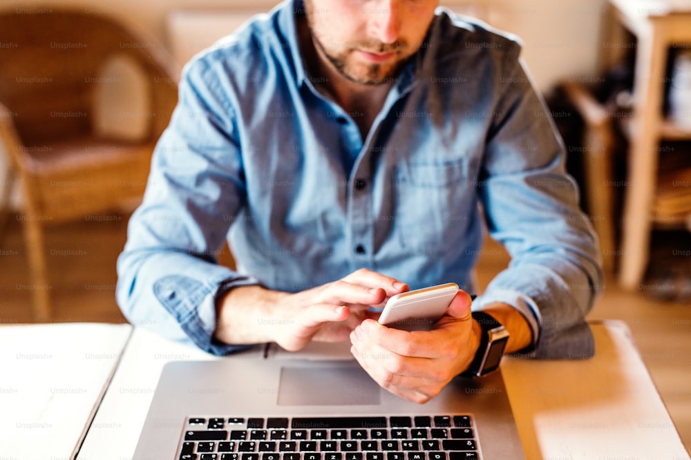 Unrecognizable man sitting at the desk working from home on computer and smart phone