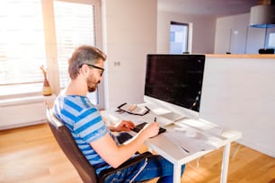 机に座って、自宅でコンピュータを使って仕事をしている男性、グラフィックタブレットを使う