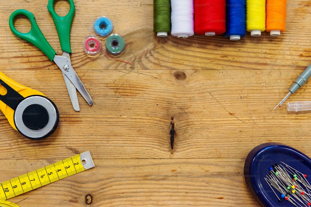 Desk of a tailor with scissors, colorful threads, pins, tape measure an other objects, flat lay, copy space