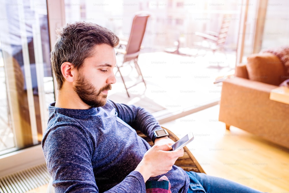 Casual hipster man working from home using smart watch, sitting in living room