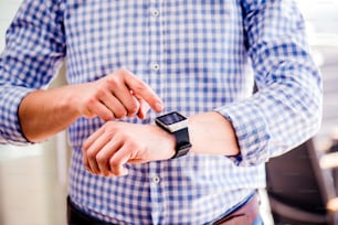 Close up of unrecognizable man in blue checked shirt using smart watch