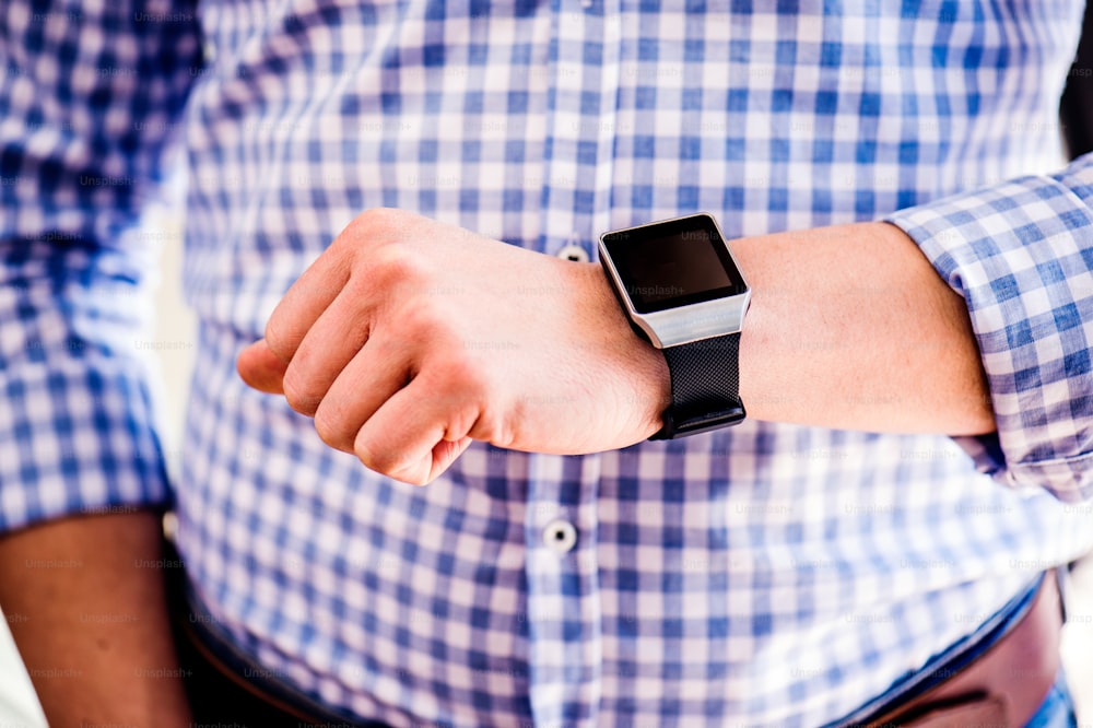 Close up of unrecognizable man in blue checked shirt using smart watch