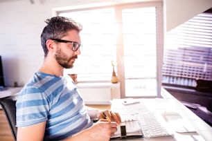 Young hipster architect working from home on computer, writing into personal organizer, taking notes