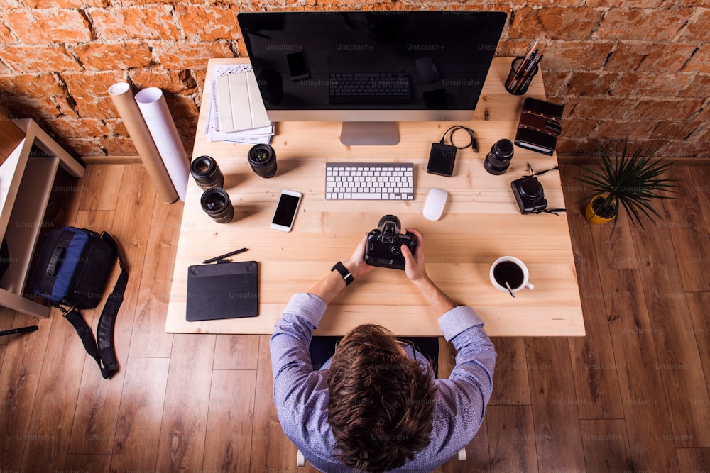 Fotógrafo na mesa, usando relógio inteligente, trabalhando com câmera.  Computador, smartphone e várias lentes de objetos ao redor do local de trabalho.