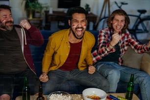 Felices amigos fanáticos del fútbol alemán viendo fútbol en casa y comiendo las palomitas de maíz.
