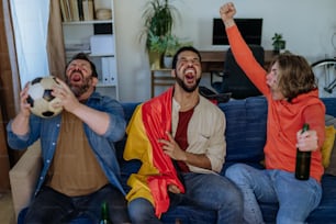 Amici felici tifosi di calcio tedeschi che guardano il calcio a casa e mangiano i popcorn.