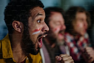 A close-up of excited football fan watching match with friends at home.