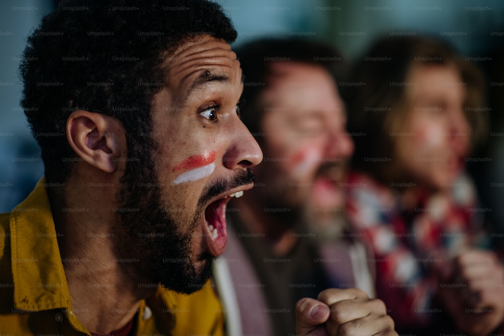 A close-up of excited football fan watching match with friends at home.