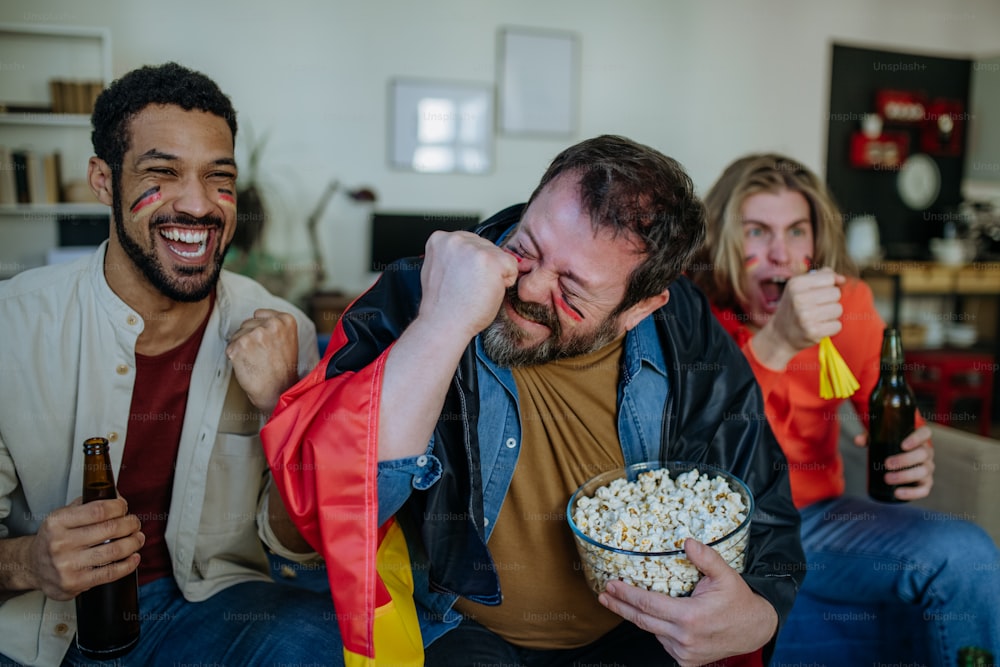 幸せなドイツのサッカーファンの友達は家でサッカーを見てポップコーンを食べます。