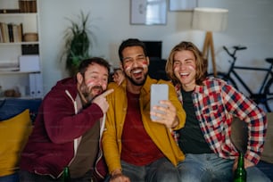 Amigos felices de los fanáticos del fútbol austriaco viendo fútbol en casa y tomándose una selfie