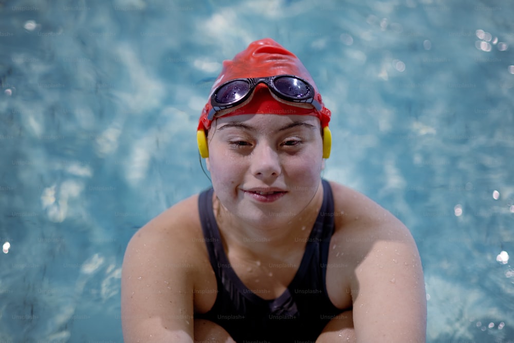 Uma mulher jovem com síndrome de Down nadando na piscina e olhando para a câmera