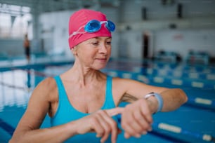 Una mujer mayor configurando un reloj inteligente antes de nadar en la piscina cubierta.