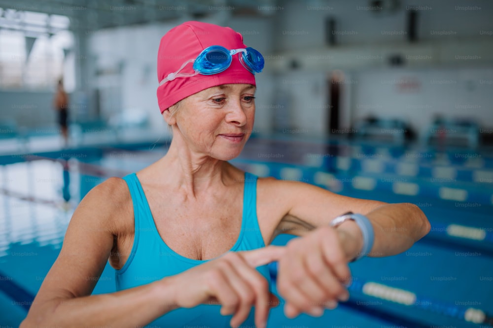 Une femme âgée installant une montre intelligente avant de nager dans une piscine intérieure.