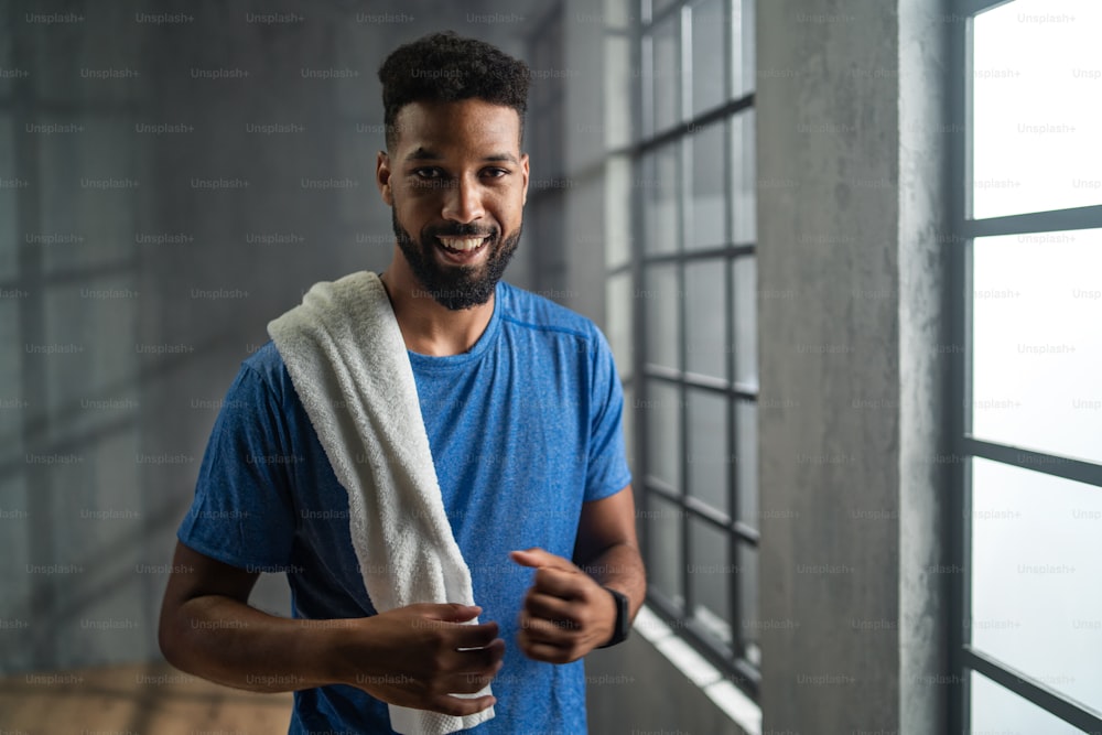 Portrait of a happy young African American sportsman standing indoors at gym, looking at camera, workout training concept.