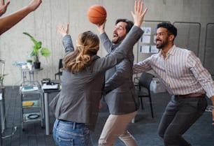 Um grupo de jovens empresários alegres jogando basquete no escritório, fazendo uma pausa no conceito.
