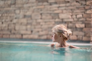 Portrait of happy senior woman in indoor swimming pool, standing.