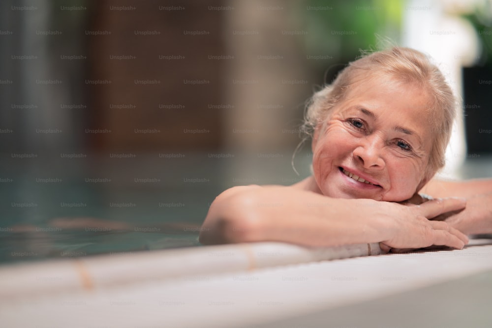 Portrait of happy senior woman in indoor swimming pool, looking at camera.