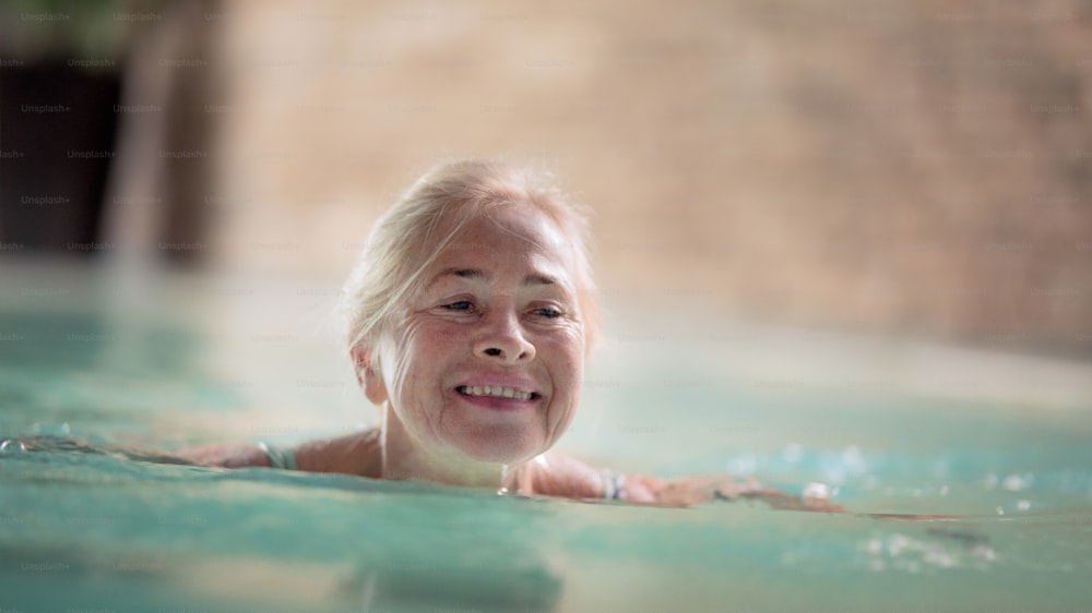 실내 수영장에서 수영하는 행복한 노인 여성의 초상화.