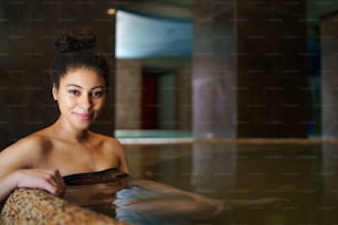 Portrait of happy young woman in indoor hot spring thermal pool, looking at camera.