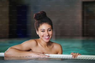 Portrait of happy young woman in indoor swimming pool, looking at camera.
