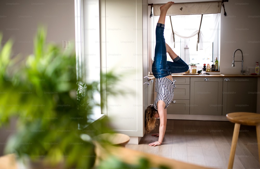 Vista lateral da jovem mulher que pratica esporte dentro de casa em casa, handstand.