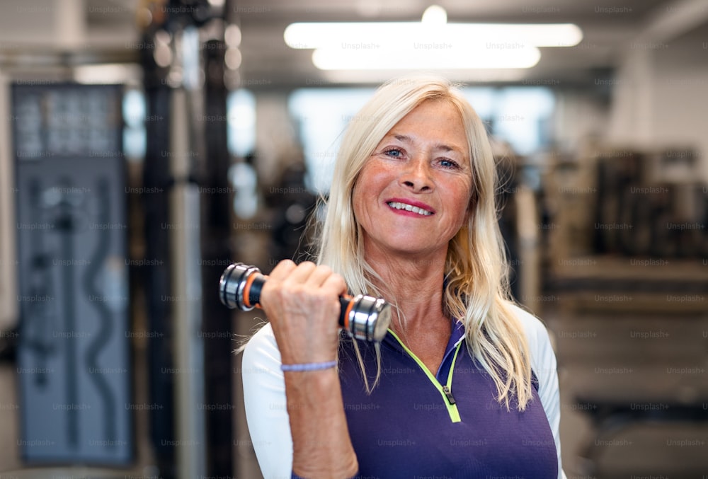 A midsection of unrecognizable senior woman with dumbbells in gym, doing exercise.
