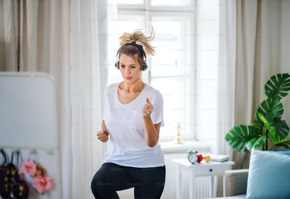 Una mujer joven con auriculares haciendo ejercicio en el dormitorio interior de su casa.