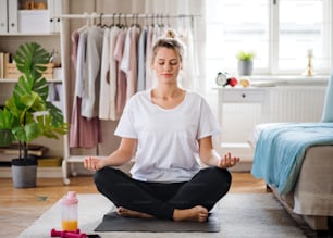 自宅の屋内でヨガの練習をし、瞑想している若い女性の正面図。