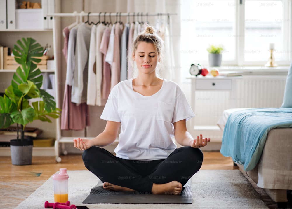 Front view of young woman doing yoga exercise indoors at home, meditating.
