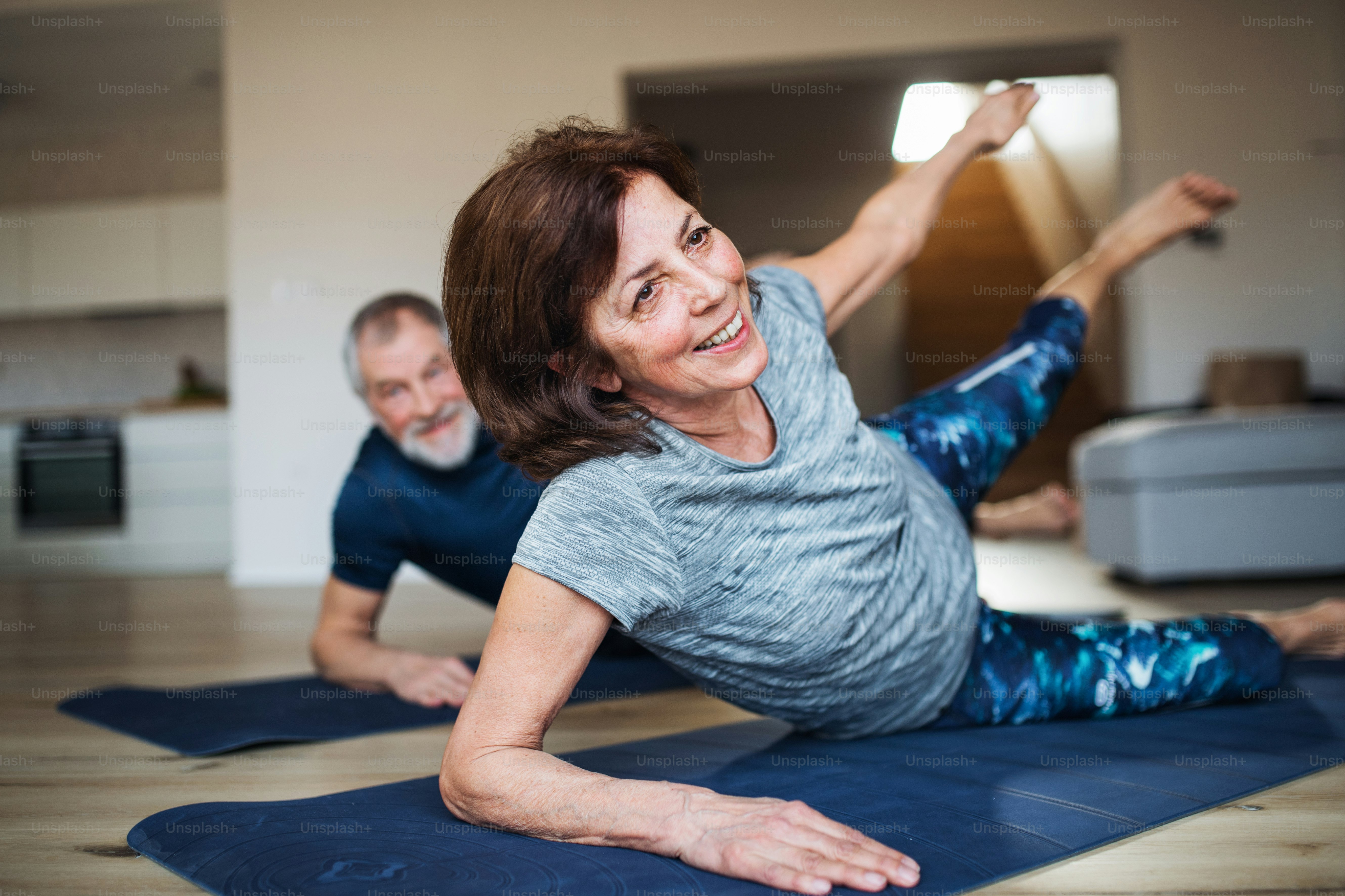 A happy senior couple indoors at home, doing exercise on the floor