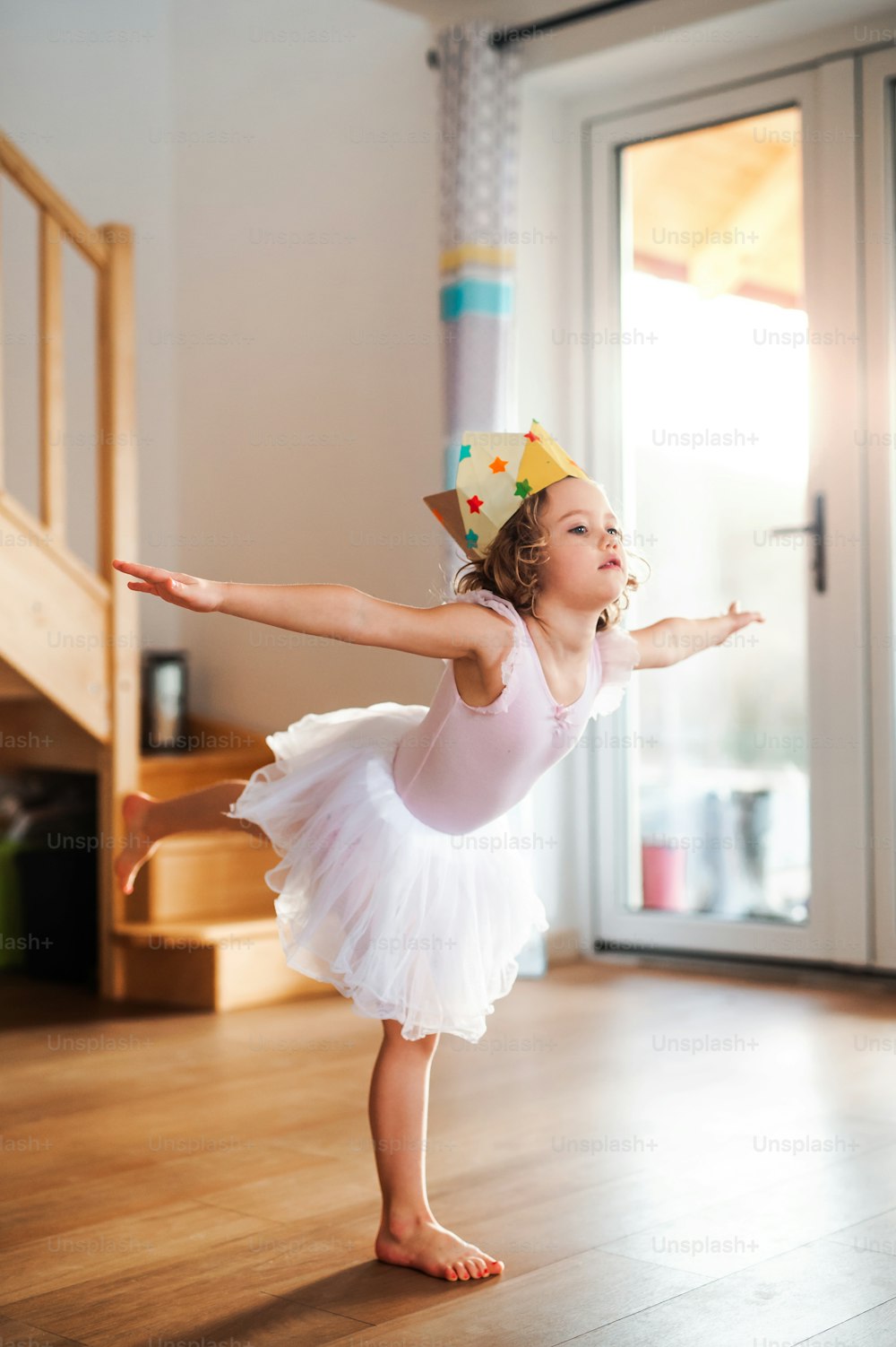 A small ballerina girl with a princess crown at home, dancing.