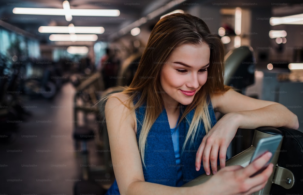 A portrait of happy young girl or woman with smartphone in a gym, taking selfie.