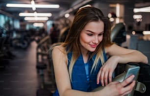 Un retrato de una niña o mujer feliz con un teléfono inteligente en un gimnasio, tomando selfie.