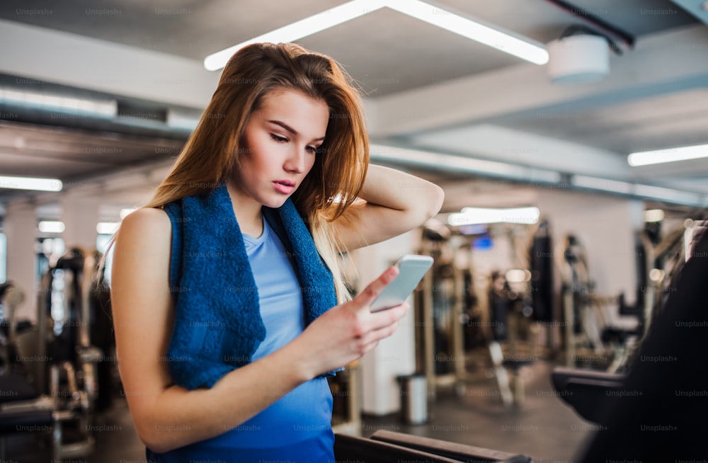A portrait of happy young girl or woman in a gym, using smartphone.