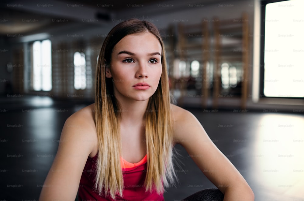 A portrait of young sad girl or woman sitting in a gym. Copy space.
