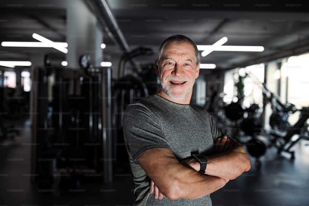 A cheerful senior man standing in gym, arms crossed. Copy space.