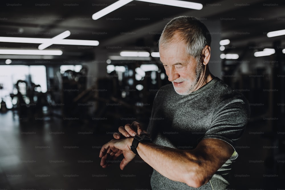 A cheerful senior man with smartwatch in gym measuring time while doing exercise. Copy space.
