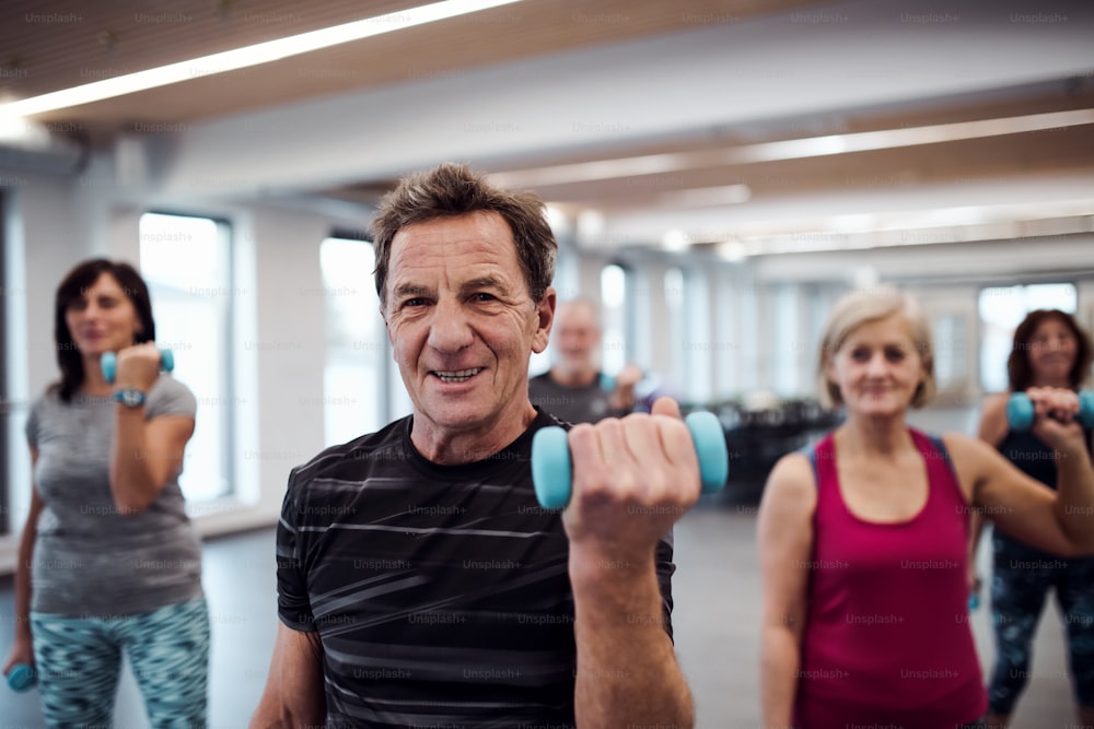 Un grupo de personas mayores alegres de pie en el gimnasio haciendo ejercicio con mancuernas.