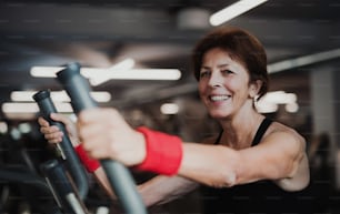 Una mujer mayor alegre en el gimnasio haciendo entrenamiento cardiovascular, haciendo ejercicio en bicicleta estacionaria.