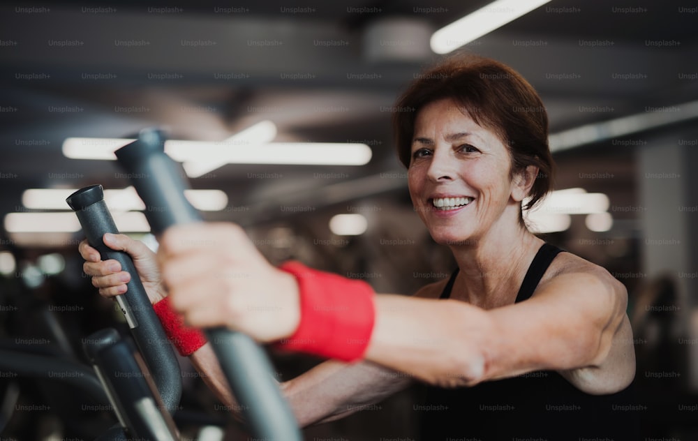 A cheerful female senior in gym doing cardio workout, exercising on stationary bicycle.