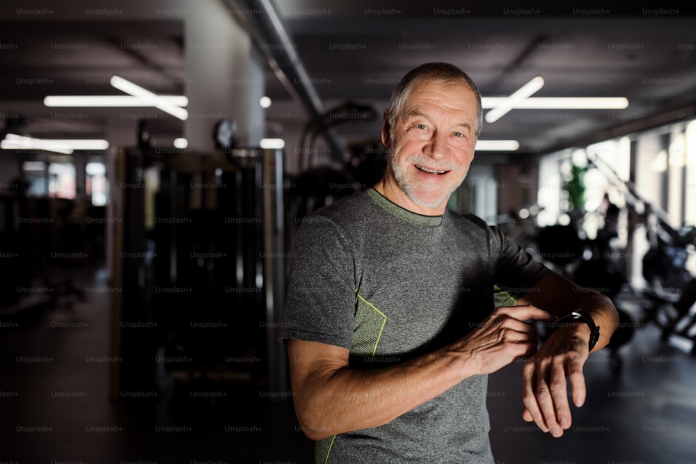 A cheerful senior man with smartpwatch in gym measuring time while doing exercise. Copy space.