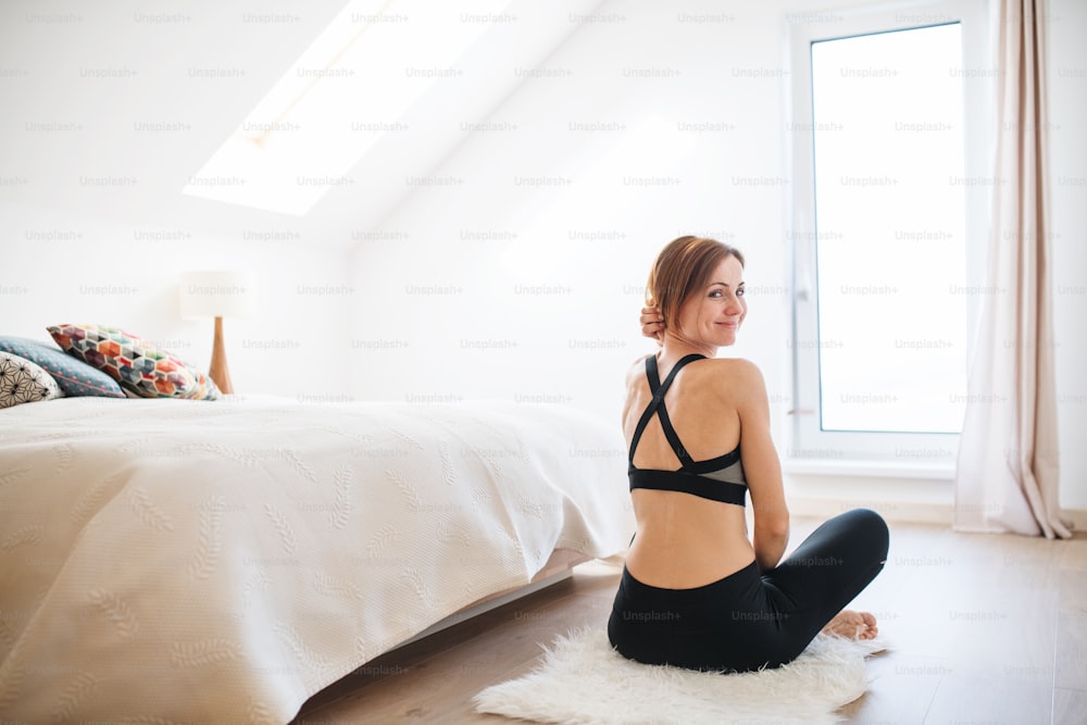 A rear view of young woman doing yoga exercise indoors in a bedroom. Copy space.