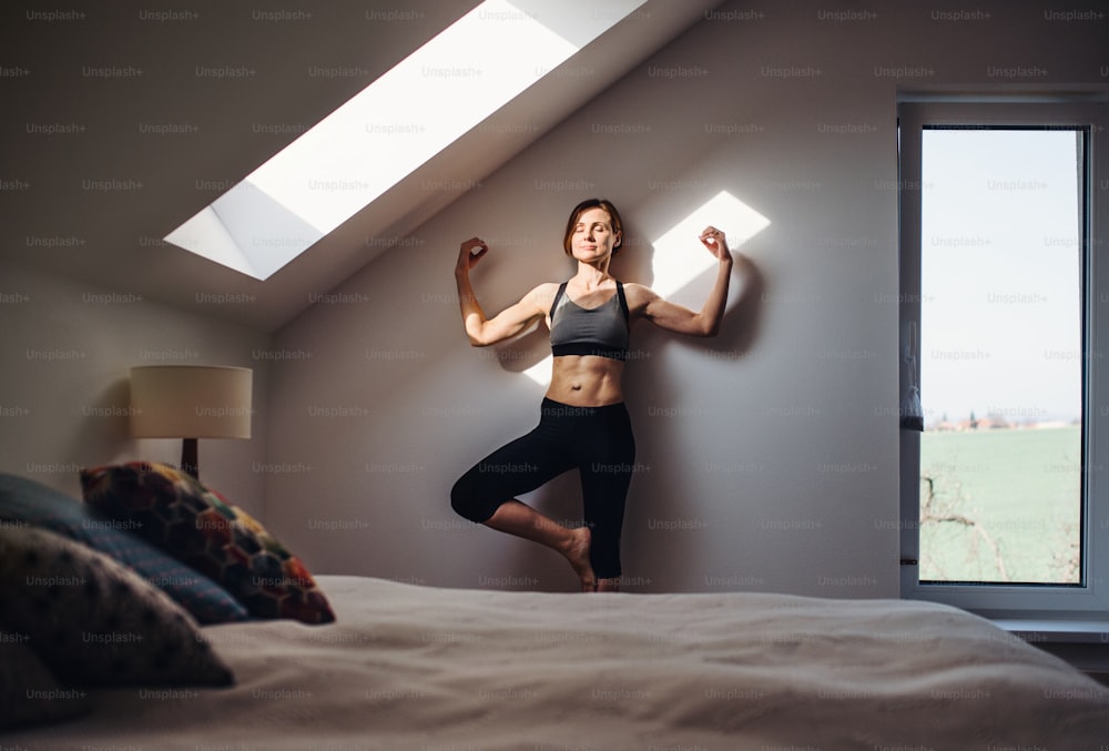 A front view of young woman doing yoga exercise indoors in a bedroom. Copy space.