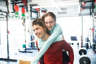 Young fit couple in modern gym. Man carrying woman on his shoulders.