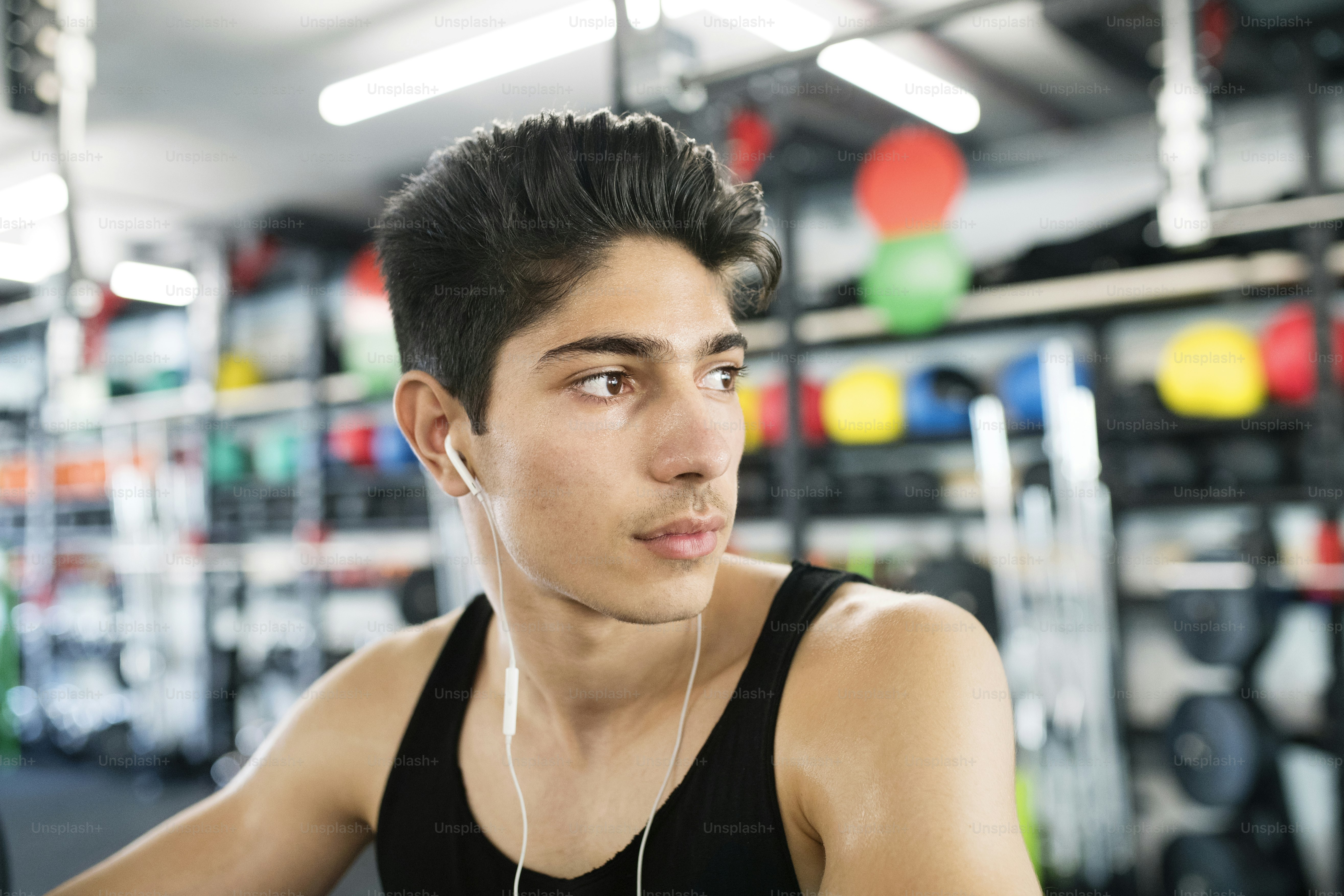 Hombre hispano en el gimnasio en la barra pesada, descansando, auriculares en los oídos, escuchando música