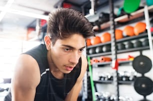 Young fit hispanic man in black sleeveless shirt in modern gym gym resting