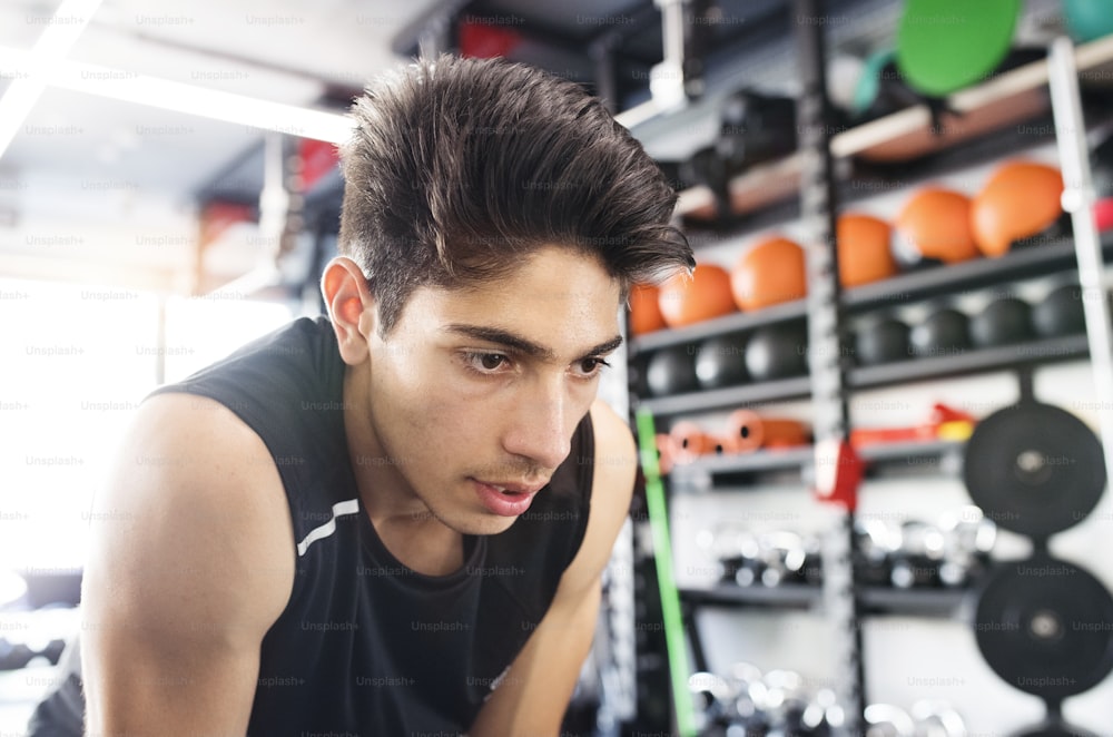 Jovem homem hispânico em forma de camisa preta sem mangas no ginásio moderno de descanso