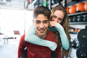 Young fit couple in modern gym gym. Man carrying woman on his shoulders.