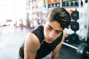 Young fit hispanic man in black sleeveless shirt in modern gym gym resting
