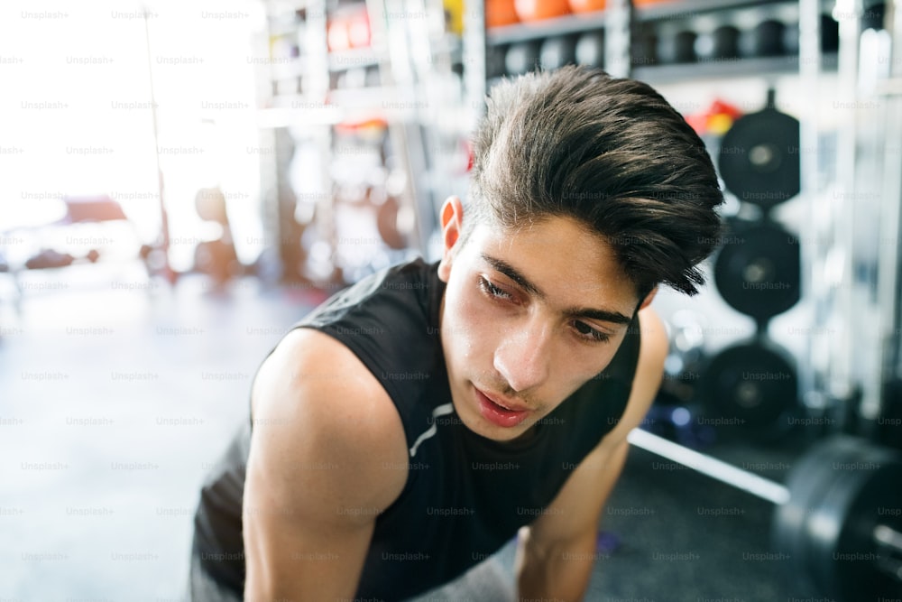 Young fit hispanic man in black sleeveless shirt in modern gym gym resting